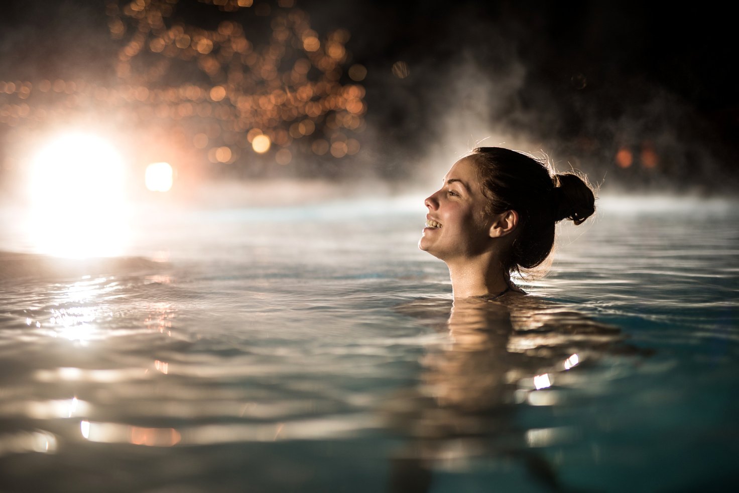 Happy woman spending a winter night in heated swimming pool.